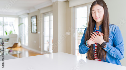 Young beautiful asian woman with long hair wearing denim jacket smiling with hands on chest with closed eyes and grateful gesture on face. Health concept.