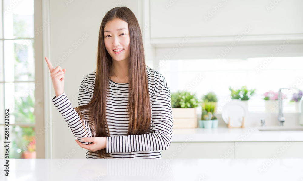 Beautiful Asian woman wearing stripes sweater with a big smile on face, pointing with hand and finger to the side looking at the camera.