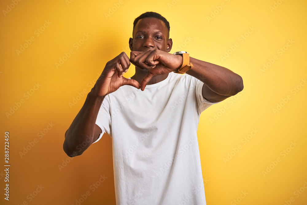 Young african american man wearing white t-shirt standing over isolated yellow background smiling in love doing heart symbol shape with hands. Romantic concept.