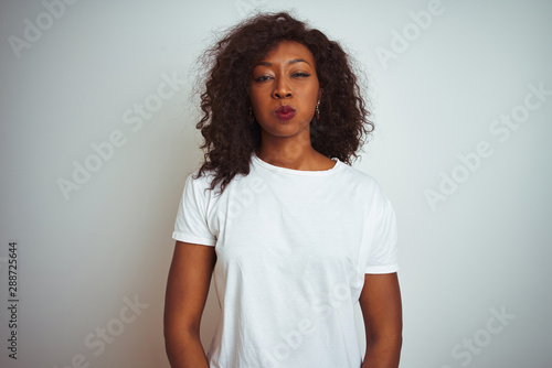 Young african american woman wearing t-shirt standing over isolated white background puffing cheeks with funny face. Mouth inflated with air, crazy expression.