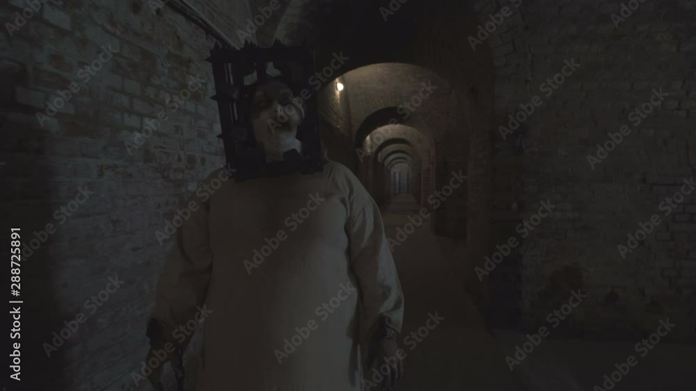 A scary ghost of a fat woman with a rusty cage on his head and with shackles on his hands wanders through the gloomy corridors of old dungeons. A scary ghost of a fat woman with a rusty cage on his head and with shackles on his hands wanders through the gloomy corridors of old dungeons.