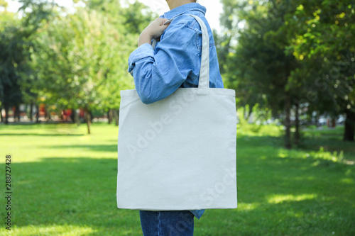 Young woman holding tote bag against greenery background, empty space