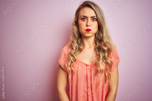 Young beautiful woman wearing t-shirt standing over pink isolated background puffing cheeks with funny face. Mouth inflated with air, crazy expression.