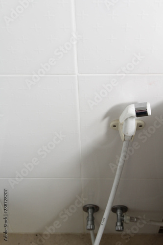 Bathroom interior and bidet shower, bidet spray, toilet nozzle, water bidet, rinsing spray on the white wall with tank of toilet bowl.