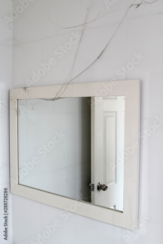White plastic frame mirror and cobwebs on white tiles wall.