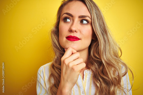 Young beautiful woman wearing stripes shirt standing over yellow isolated background serious face thinking about question, very confused idea