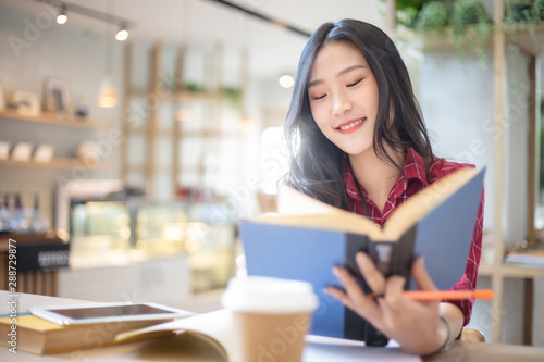 Young beautiful Asian woman reading a book while doing her homework in the modern co working space