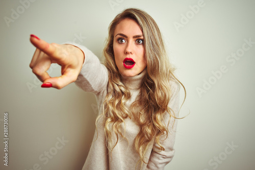 Beautiful woman wearing winter turtleneck sweater over isolated white background Pointing with finger surprised ahead, open mouth amazed expression, something on the front