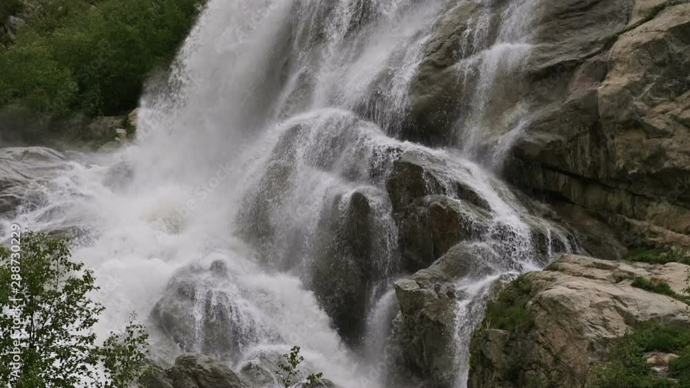Slow motion water falls from a huge rock. Waterfall in the natural environment in cloudy weather with light rain Slow motion water falls from a huge rock. Waterfall in the natural environment in cloudy weather with light rain