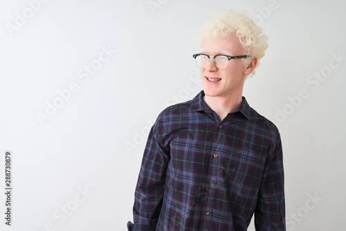 Young albino blond man wearing casual shirt and glasses over isolated white background looking away to side with smile on face, natural expression. Laughing confident.