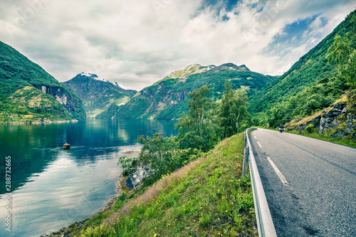 Riding a motorcycle on the road on the shore of Sunnylvsfjorden fjord. Colorful morning view of western Norway, Europe. Traveling concept background. Instagram filter toned.