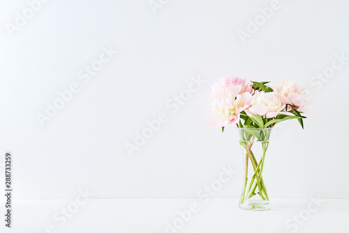 Pink and white peonies in a glass vase on a white background