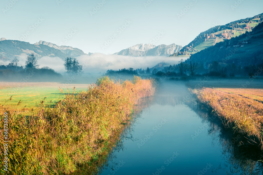 Fototapeta Sunny morning scene near Zell lake. Foggy autumn view of Austrian Alps. Beauty of nature concept background. Instagram filter toned.