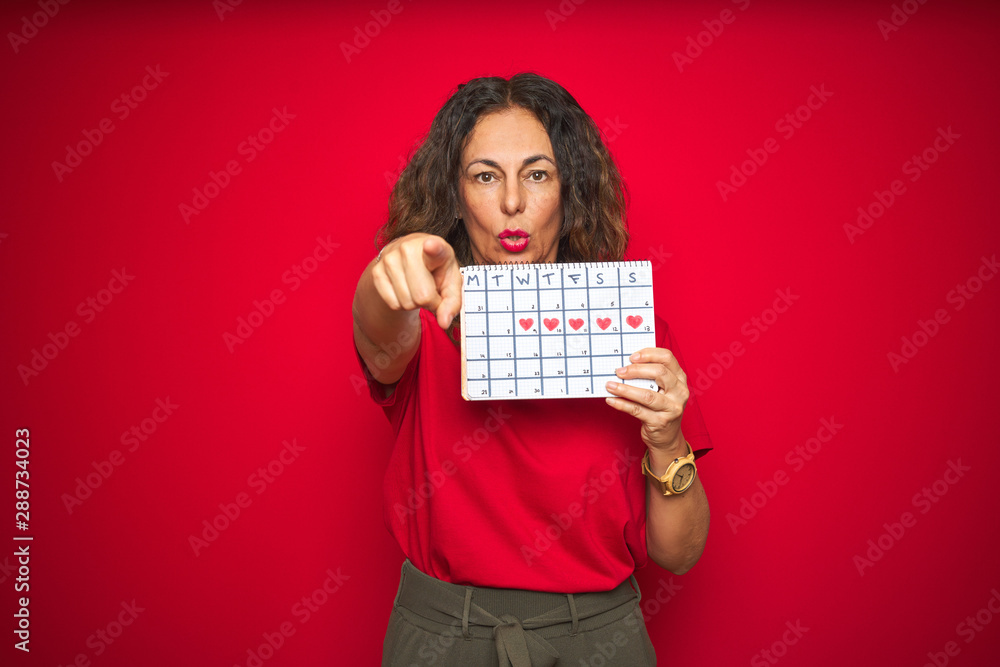 Middle age senior woman holding menstruation calendar over red isolated background pointing with finger to the camera and to you, hand sign, positive and confident gesture from the front Middle age senior woman holding menstruation calendar over red isolated background pointing with finger to the camera and to you, hand sign, positive and confident gesture from the front