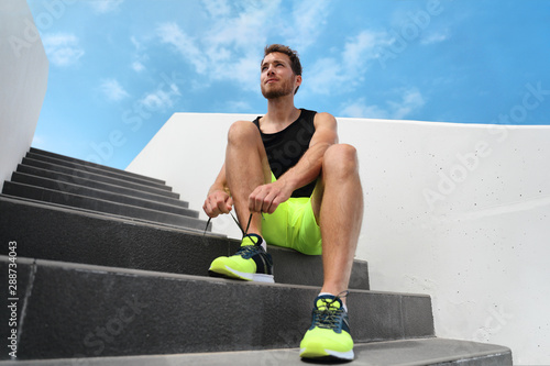 Runner man getting ready to train outdoor on city stairs gym outside tying running shoes laces training cardio workout exercise on staircase. Acitve healthy lifestyle sport athlete fitness motivation. photo