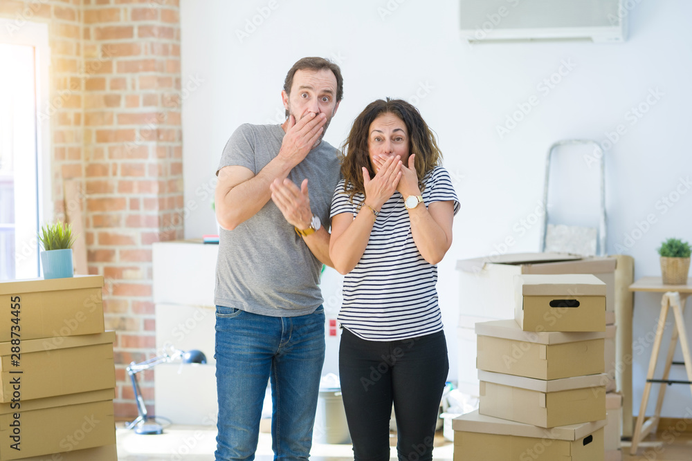 Middle age senior couple moving to a new home with boxes around shocked covering mouth with hands for mistake. Secret concept. Middle age senior couple moving to a new home with boxes around shocked covering mouth with hands for mistake. Secret concept.
