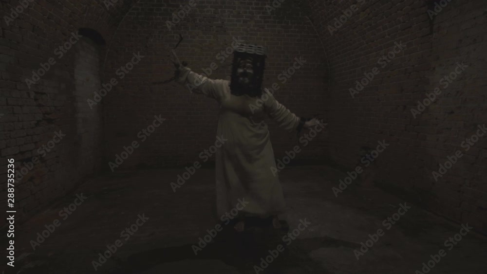 A funny ghost of a fat woman with a rusty cage on his head and with shackles on his hands dances in the gloomy room of old dungeon. A funny ghost of a fat woman with a rusty cage on his head and with shackles on his hands dances in the gloomy room of old dungeon.