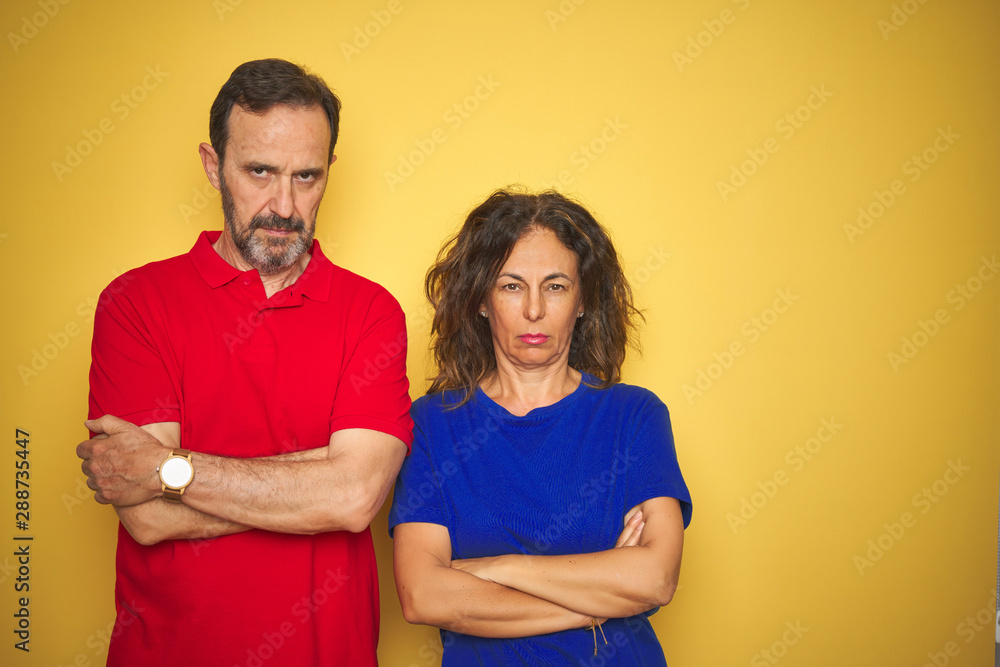 Obraz premium Beautiful middle age couple together standing over isolated yellow background skeptic and nervous, disapproving expression on face with crossed arms. Negative person.