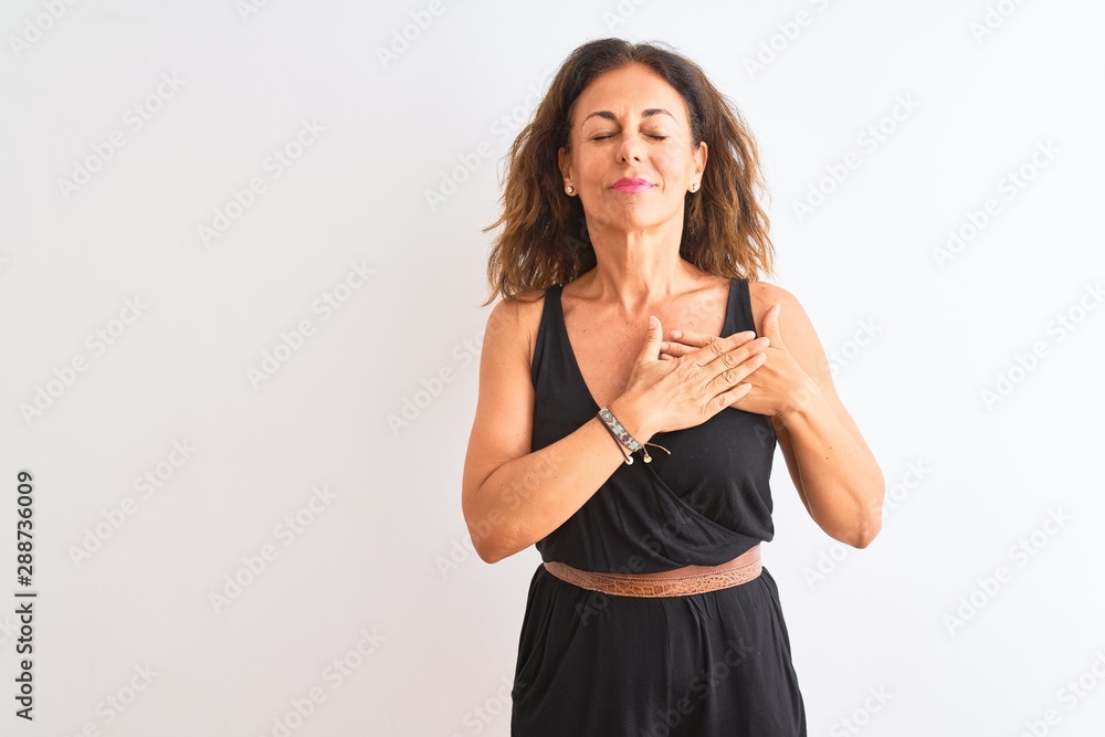 Middle age woman wearing black casual dress standing over isolated white background smiling with hands on chest with closed eyes and grateful gesture on face. Health concept. Middle age woman wearing black casual dress standing over isolated white background smiling with hands on chest with closed eyes and grateful gesture on face. Health concept.