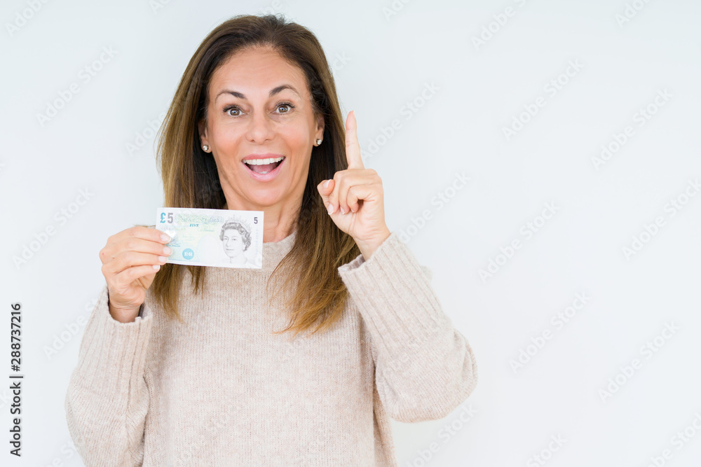 Middle age woman holding 5 pounds bank note over isolated background surprised with an idea or question pointing finger with happy face, number one Middle age woman holding 5 pounds bank note over isolated background surprised with an idea or question pointing finger with happy face, number one