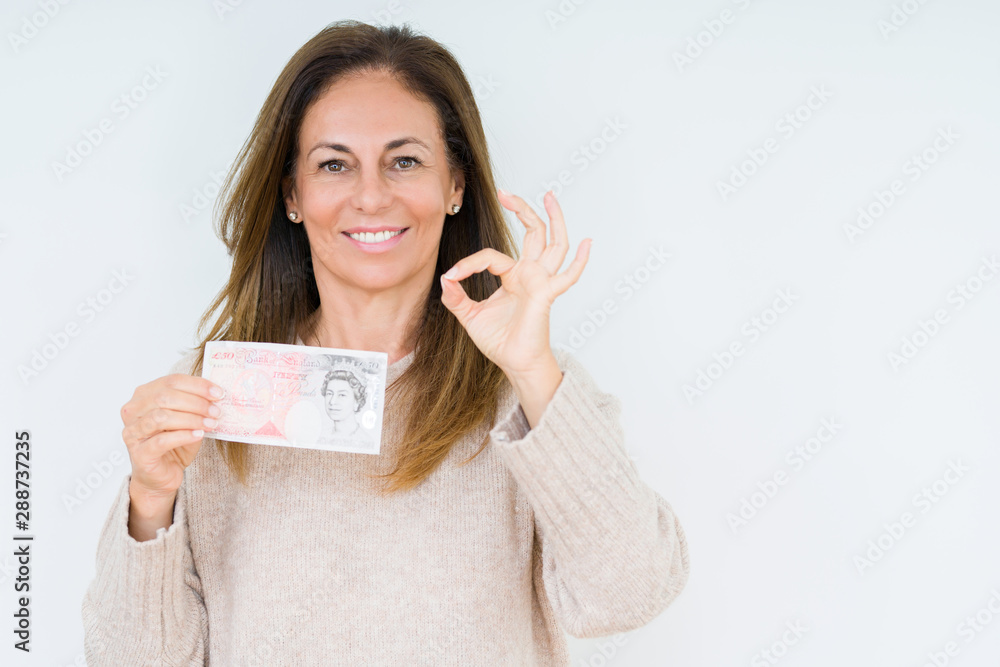 Middle age woman holding 50 pounds bank note over isolated background doing ok sign with fingers, excellent symbol Middle age woman holding 50 pounds bank note over isolated background doing ok sign with fingers, excellent symbol