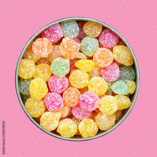colorful multicolored sucking sweets Montpensier lollipops in a round tin box isolated on a pink background close-up top view flat lay