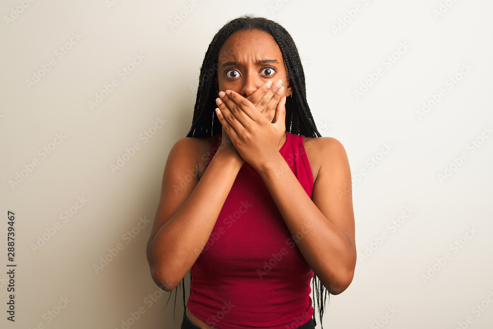 African american woman wearing red casual t-shirt standing over isolated white background shocked covering mouth with hands for mistake. Secret concept. African american woman wearing red casual t-shirt standing over isolated white background shocked covering mouth with hands for mistake. Secret concept.