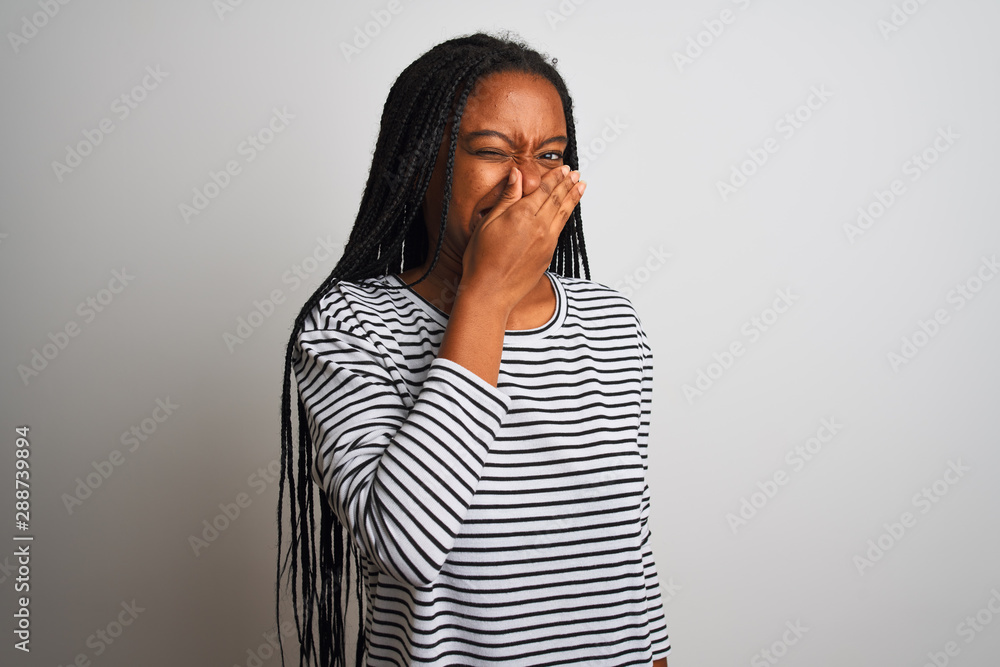 Young african american woman wearing striped t-shirt standing over isolated white background smelling something stinky and disgusting, intolerable smell, holding breath with fingers on nose. Young african american woman wearing striped t-shirt standing over isolated white background smelling something stinky and disgusting, intolerable smell, holding breath with fingers on nose.