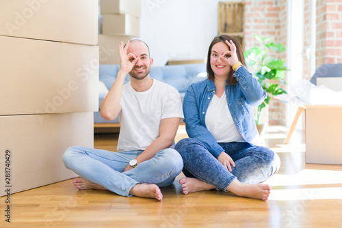 Young couple sitting on the floor arround cardboard boxes moving to a new house doing ok gesture with hand smiling, eye looking through fingers with happy face. © Krakenimages.com
