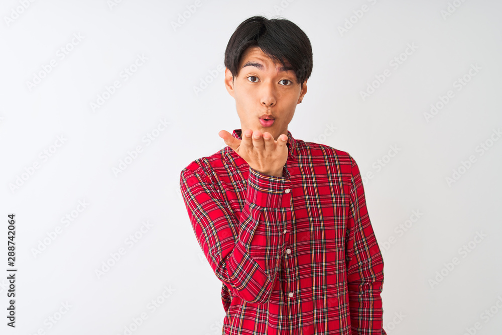 Young chinese man wearing casual red shirt standing over isolated white background looking at the camera blowing a kiss with hand on air being lovely and sexy. Love expression.