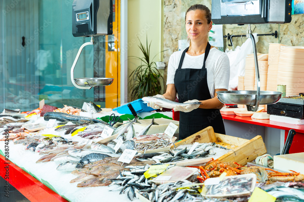 Polite female fishmonger offering fresh sea bass