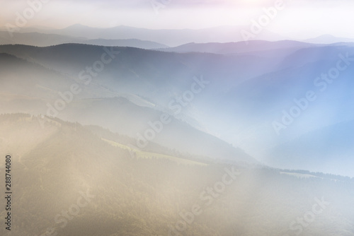 Landscape of mountain range with visible silhouettes through the morning colorful fog. Sunrise in the mountains. Filtered image:cross processed retro effect. Perfect nature background pictures.
