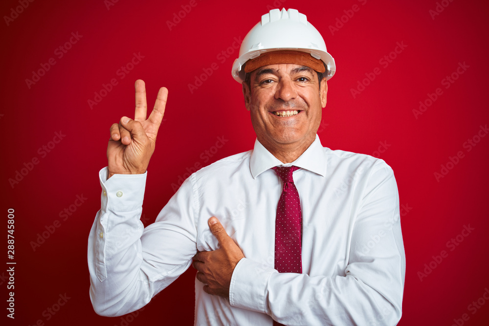 Handsome middle age engineer man wearing security helmet over isolated red background smiling with happy face winking at the camera doing victory sign. Number two. Handsome middle age engineer man wearing security helmet over isolated red background smiling with happy face winking at the camera doing victory sign. Number two.