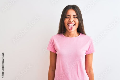 Canvas Print Young beautiful woman wearing pink casual t-shirt standing over isolated white background sticking tongue out happy with funny expression