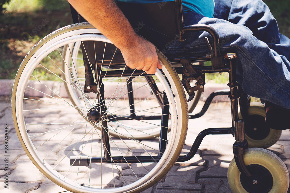 Fototapeta premium Close up photo of Young disabled man holding wheelchair outside in park
