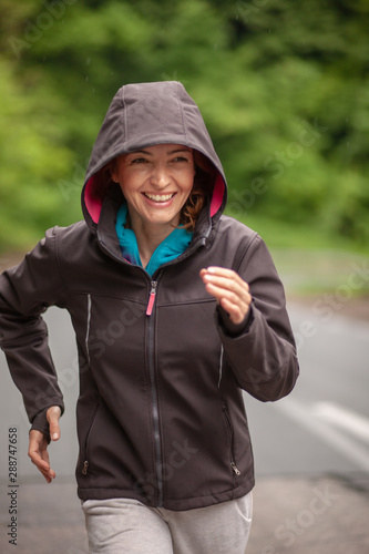 One smiling mature woman, running outdoors on a asphalt road, in a nature.