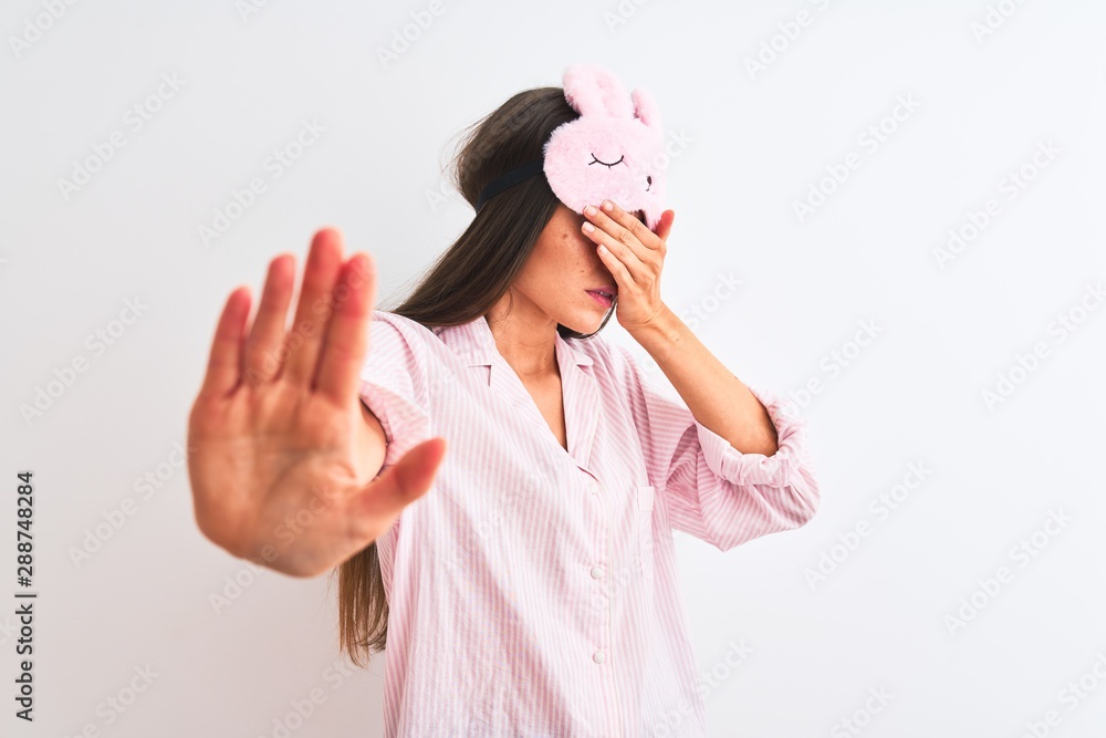 Young beautiful woman wearing sleep mask and pajama over isolated white background covering eyes with hands and doing stop gesture with sad and fear expression. Embarrassed and negative concept.