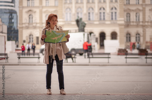 One mature woman, in old European city, holding a city map in her hands, while searching in it.