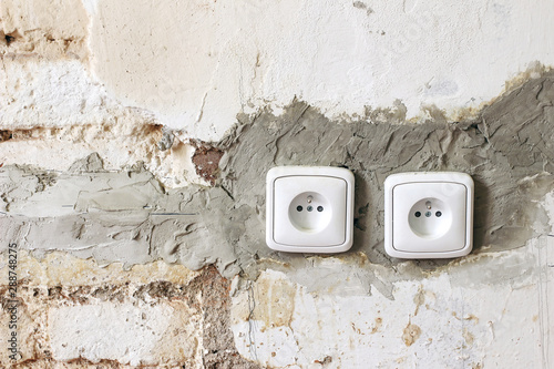 Couple of electric power plug sockets on old white dirty brick wall. Electricity repair and reconstruction concept. Vintage grunge background. Home under construction.