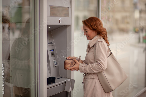 One mature woman, using ATM machine, putting credit card in her wallet.