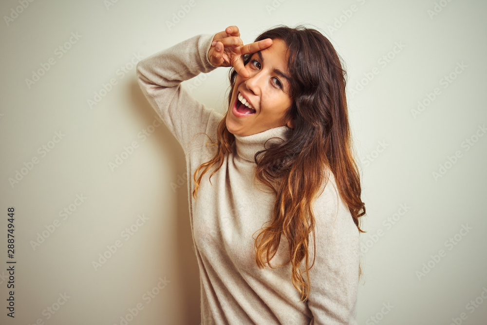 Young beautiful woman wearing winter sweater standing over white isolated background Doing peace symbol with fingers over face, smiling cheerful showing victory Young beautiful woman wearing winter sweater standing over white isolated background Doing peace symbol with fingers over face, smiling cheerful showing victory