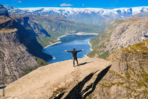 A man stands with his arms wide open with pleasure and waits for him to be photographed on the famous Trolltung rock in Norway