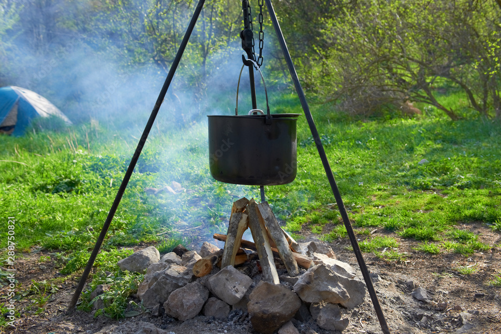 Pot boiling on fire in fireplace in forest Pot boiling on fire in fireplace in forest