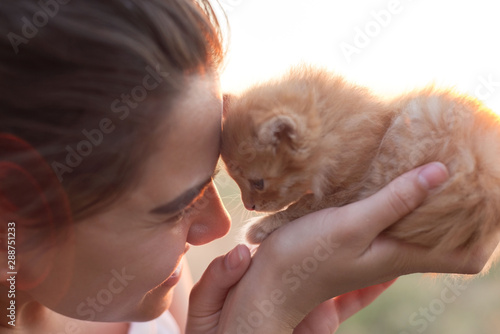 Young beautiful smiling girl holds a small kitten in her arms and presses him to his face. The concept of love and kindness. In warm colors