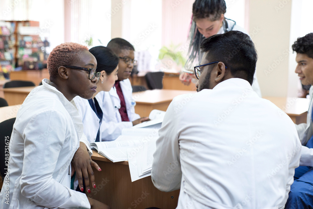 Obraz premium doctor of medicine. A group of young people of mixed race, sitting at a table in the office of the hospital, read medical literature