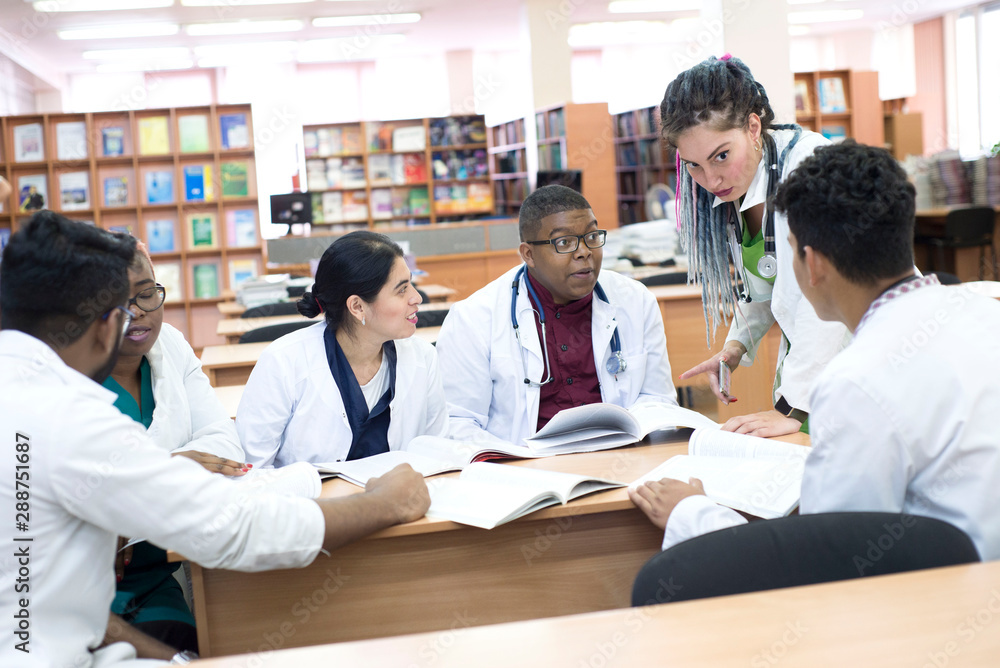 doctor of medicine. A group of young people of mixed race, sitting at a table in the office of the hospital, read medical literature