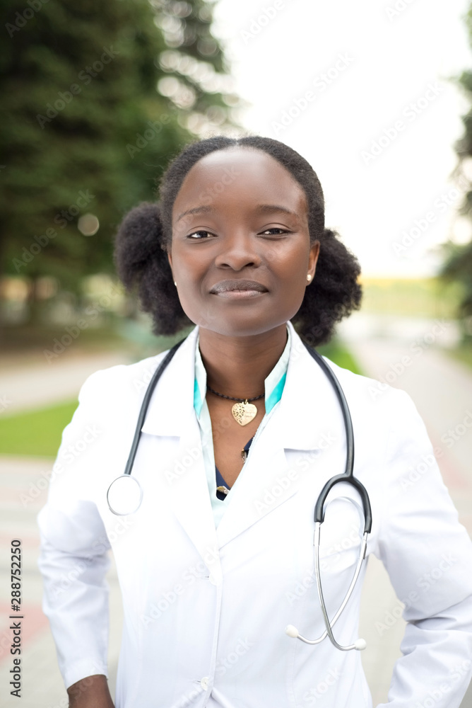 Portrait of a cute african american young girl. Doctor in a white coat, with a phonendoscope, smile, on the street Portrait of a cute african american young girl. Doctor in a white coat, with a phonendoscope, smile, on the street