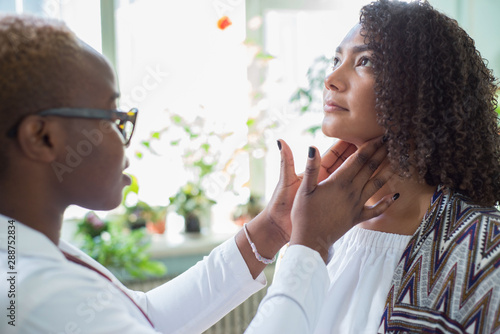 An African American female doctor examines with her fingers, palpates her neck and lymph nodes. Pain in the neck. Mixed race doctor and patient