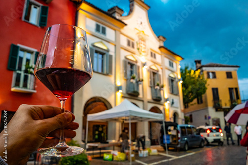 hand holding a glass of red wine in the town of Neive, Italy, one of the main villages of the Langhe hills, famous district of Barolo and Barbaresco wine. photo