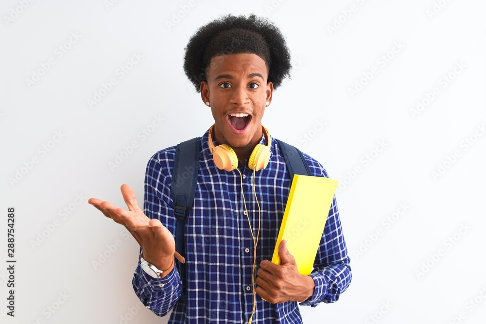 African american student man wearing headphones backpack over isolated white background very happy and excited, winner expression celebrating victory screaming with big smile and raised hands African american student man wearing headphones backpack over isolated white background very happy and excited, winner expression celebrating victory screaming with big smile and raised hands